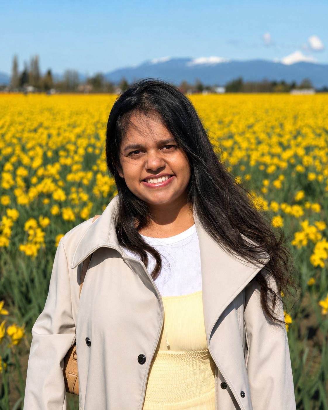 Samprithi Ravisanker smiling in a yellow flower field with mountains in the background